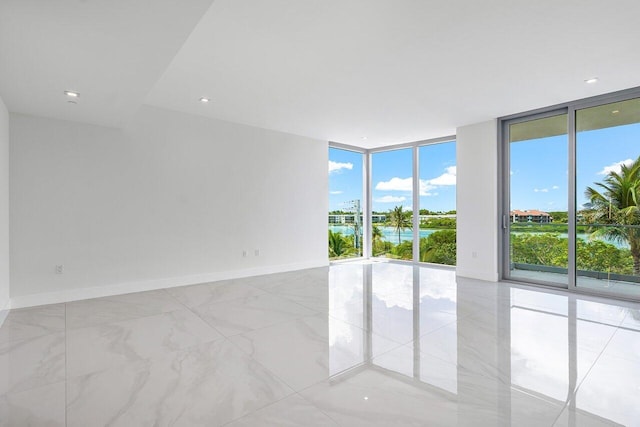 spare room featuring a healthy amount of sunlight, a wall of windows, a water view, and light tile patterned flooring