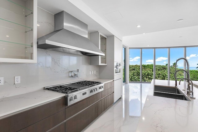 kitchen featuring wall chimney exhaust hood, stainless steel appliances, sink, decorative backsplash, and light tile patterned flooring