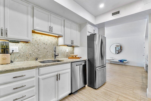 kitchen with white cabinets, appliances with stainless steel finishes, sink, backsplash, and light stone counters