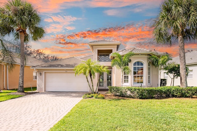 mediterranean / spanish-style home featuring a balcony, an attached garage, stucco siding, french doors, and decorative driveway