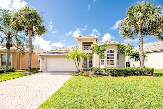 mediterranean / spanish home featuring a front lawn, stucco siding, french doors, decorative driveway, and an attached garage