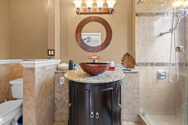 bathroom featuring tiled shower, toilet, vanity, and tile walls