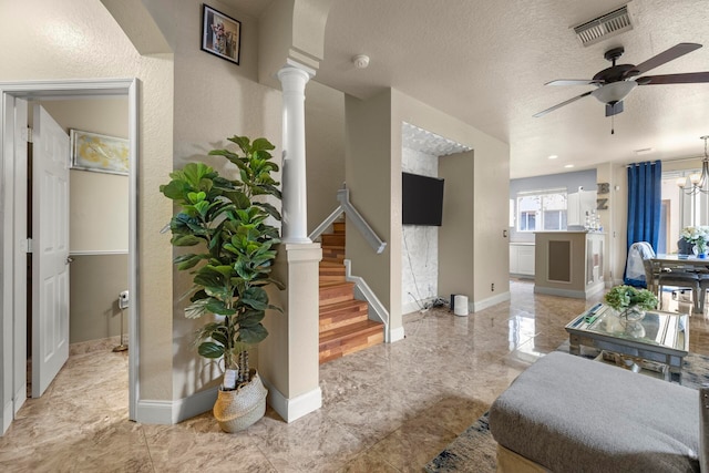 living room featuring a textured ceiling, light hardwood / wood-style flooring, ceiling fan with notable chandelier, and ornate columns