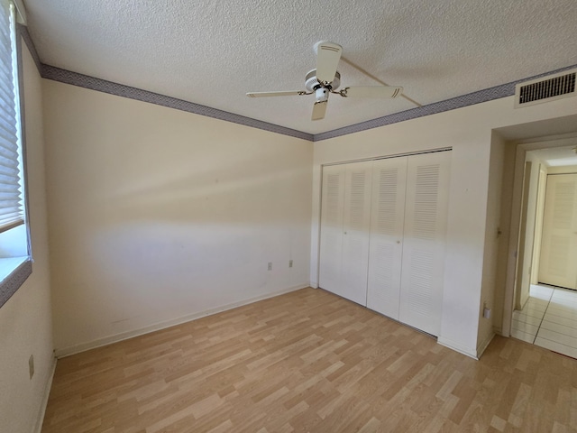 unfurnished bedroom featuring light wood-style floors, a closet, visible vents, and a textured ceiling