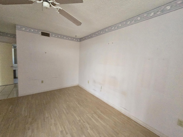 spare room with a textured ceiling, wood finished floors, visible vents, baseboards, and a ceiling fan