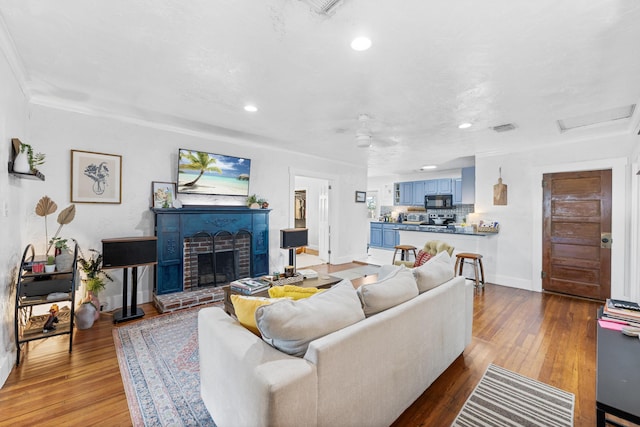 living room with ceiling fan, a brick fireplace, and light hardwood / wood-style flooring