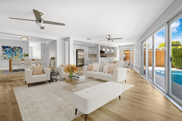 living area with light wood-style floors, ceiling fan, and baseboards