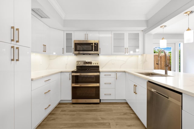 kitchen with white cabinets, hanging light fixtures, appliances with stainless steel finishes, light wood-type flooring, and sink