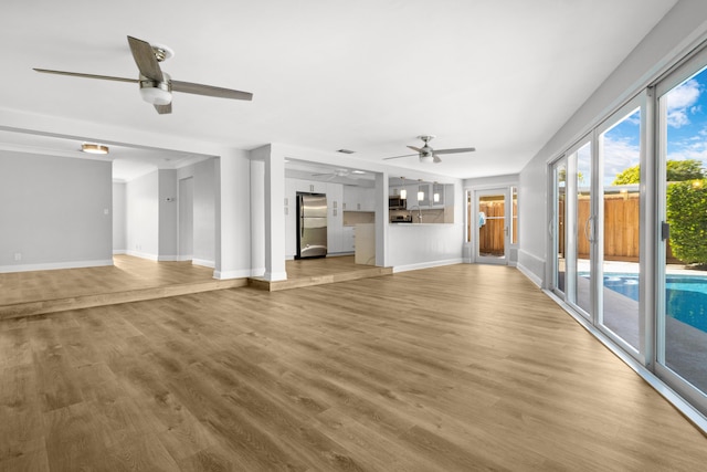 unfurnished living room with a ceiling fan, light wood-type flooring, and baseboards