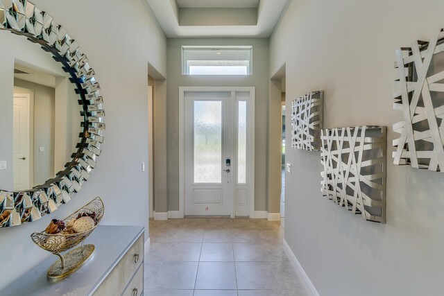 foyer with light tile patterned floors, a high ceiling, and a tray ceiling