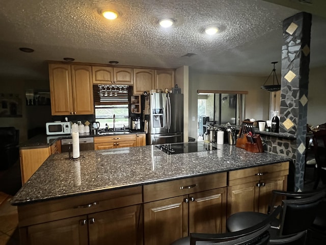 kitchen featuring sink, dark stone countertops, dishwashing machine, and stainless steel refrigerator with ice dispenser