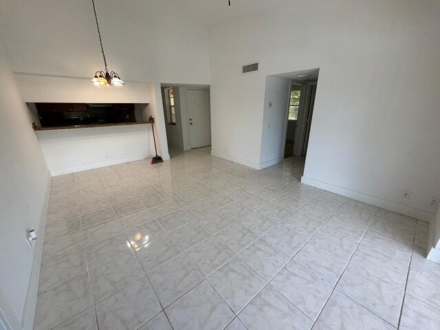 unfurnished living room featuring a high ceiling, light tile patterned flooring, and a chandelier