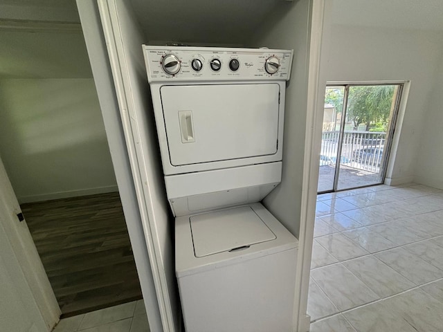 clothes washing area with laundry area, light tile patterned floors, baseboards, and stacked washer / dryer