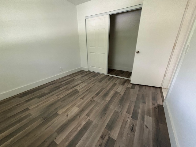 unfurnished bedroom featuring dark wood-style floors, a closet, and baseboards