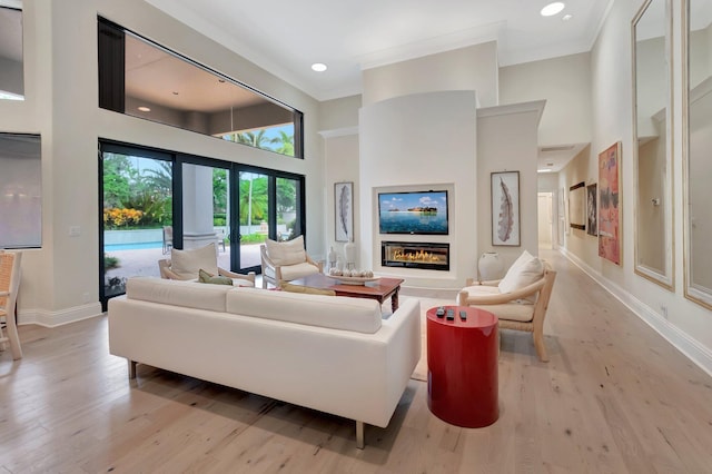 living room with a high ceiling, light hardwood / wood-style floors, ornamental molding, and french doors