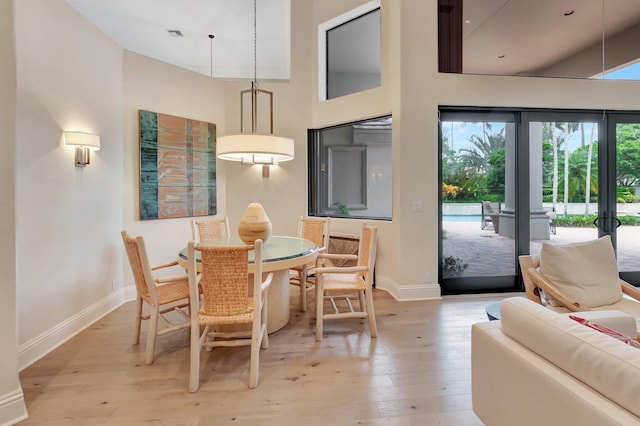 dining space featuring light wood-type flooring, a towering ceiling, and french doors