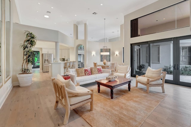 living room with light wood-type flooring, a towering ceiling, french doors, and ornate columns