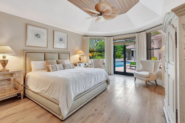 bedroom featuring multiple windows, light hardwood / wood-style flooring, access to outside, ceiling fan, and a raised ceiling