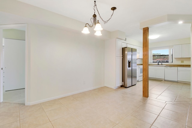 interior space with white appliances, an inviting chandelier, white cabinets, sink, and light tile patterned floors