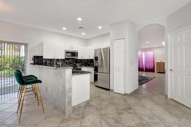 kitchen featuring arched walkways, decorative backsplash, appliances with stainless steel finishes, white cabinetry, and a peninsula