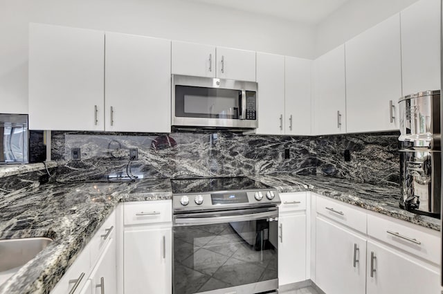 kitchen featuring tasteful backsplash, appliances with stainless steel finishes, white cabinets, a sink, and dark stone counters