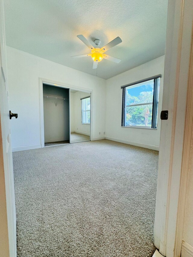 unfurnished bedroom featuring a closet, a textured ceiling, light colored carpet, and ceiling fan