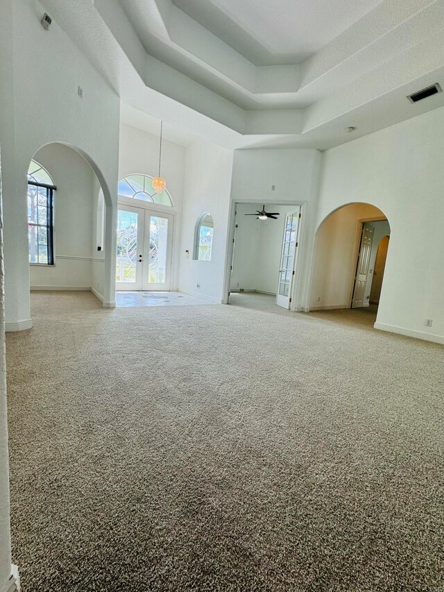 empty room with french doors, a towering ceiling, carpet floors, and ceiling fan