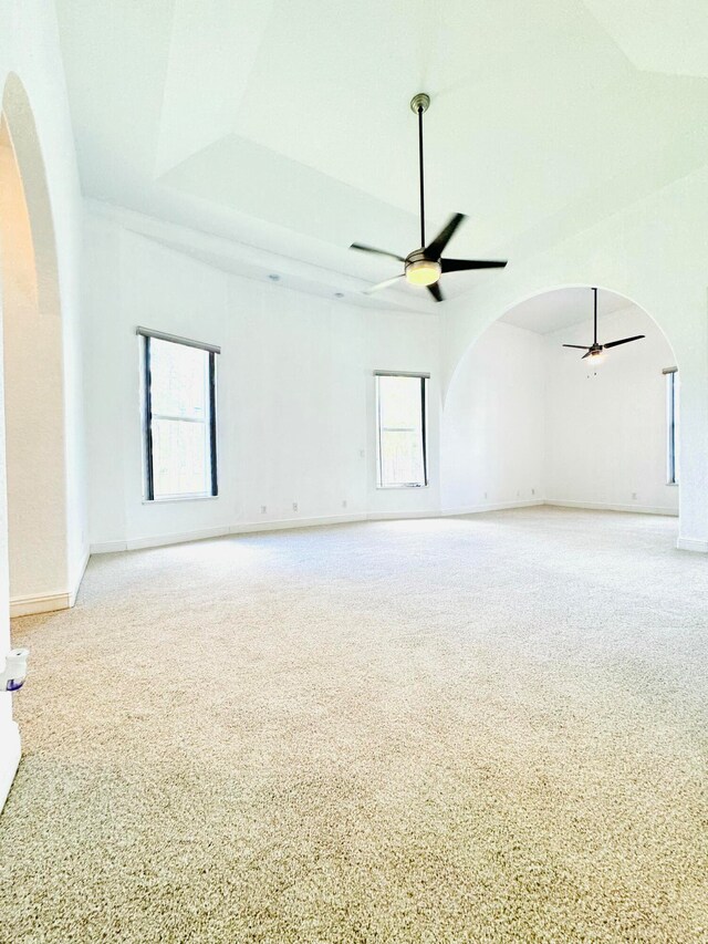 empty room with light colored carpet, ceiling fan, and a raised ceiling