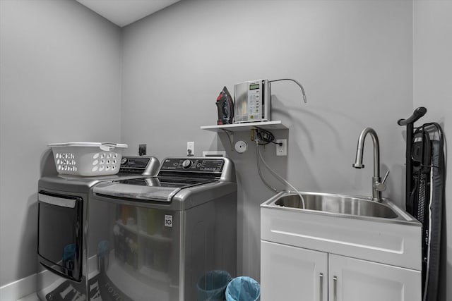 clothes washing area with washing machine and dryer, cabinets, and sink