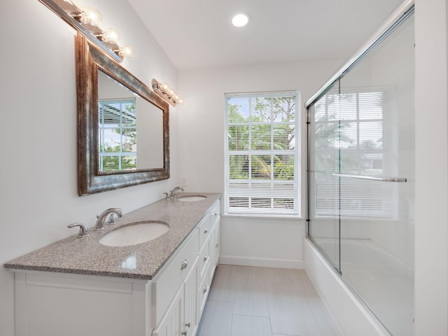 full bath featuring a healthy amount of sunlight, a sink, baseboards, and double vanity