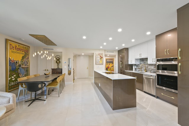 kitchen featuring backsplash, decorative light fixtures, stainless steel appliances, white cabinetry, and sink