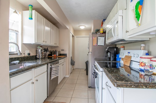 kitchen with dark stone counters, stainless steel dishwasher, light tile patterned floors, stove, and white cabinets