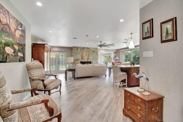 living room featuring ceiling fan, light hardwood / wood-style flooring, a large fireplace, and french doors