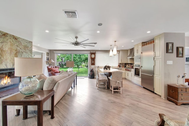 living room featuring ceiling fan, light wood-type flooring, and a large fireplace