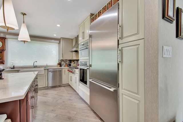 kitchen with appliances with stainless steel finishes, light hardwood / wood-style flooring, cream cabinetry, pendant lighting, and custom exhaust hood