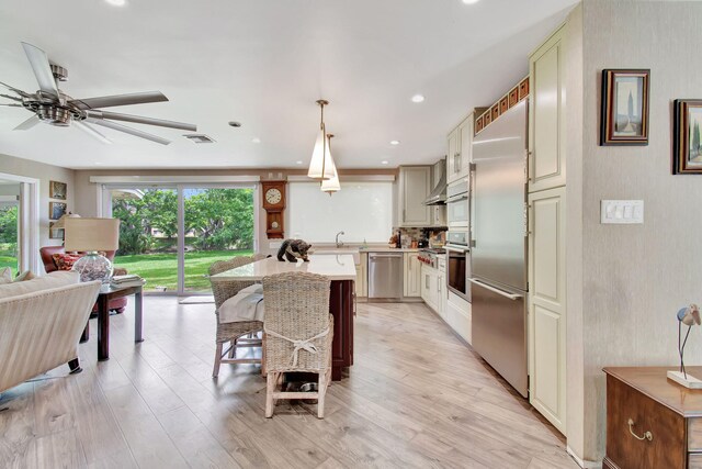 kitchen featuring light wood-type flooring, pendant lighting, cream cabinetry, and stainless steel appliances