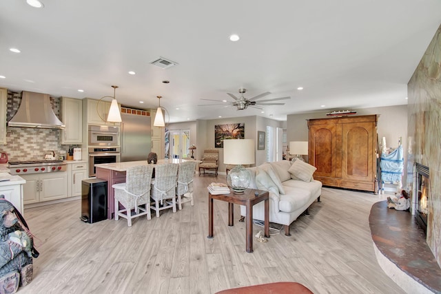 living room with light wood-type flooring, a large fireplace, and ceiling fan