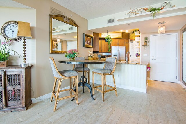 kitchen with a kitchen bar, sink, light hardwood / wood-style flooring, stainless steel fridge, and kitchen peninsula