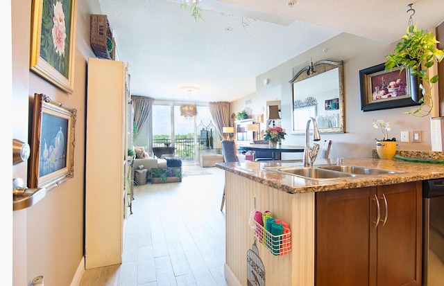 kitchen with light wood finished floors, dishwasher, open floor plan, a textured ceiling, and a sink