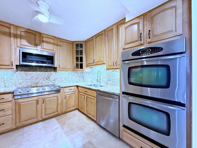 kitchen with light stone counters, sink, backsplash, and appliances with stainless steel finishes