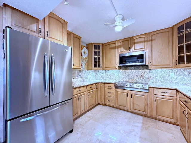 kitchen featuring light stone counters, ceiling fan, stainless steel appliances, and decorative backsplash