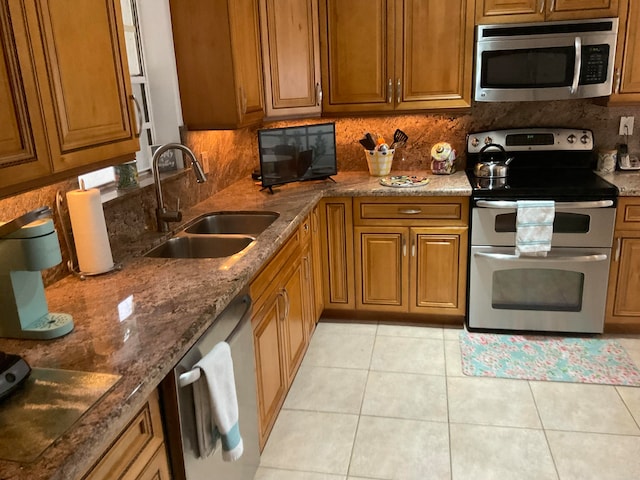 kitchen featuring backsplash, light tile patterned floors, dark stone countertops, sink, and stainless steel appliances