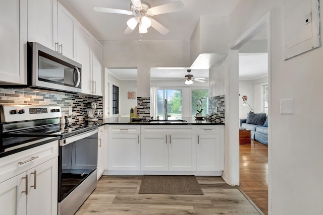 kitchen with stainless steel appliances, a sink, light wood-type flooring, backsplash, and dark countertops