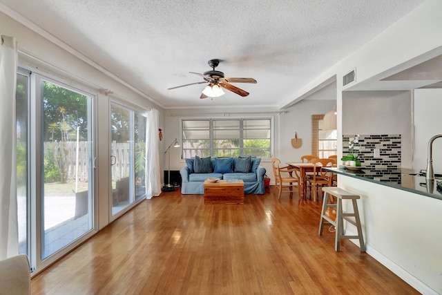 living room featuring ceiling fan, light wood-type flooring, and a textured ceiling