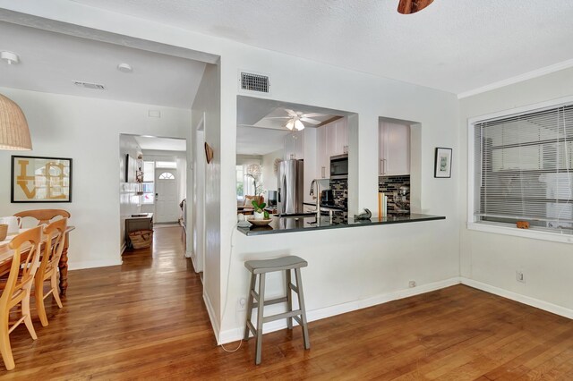 kitchen with ceiling fan, wood-type flooring, white cabinets, a breakfast bar area, and stainless steel appliances