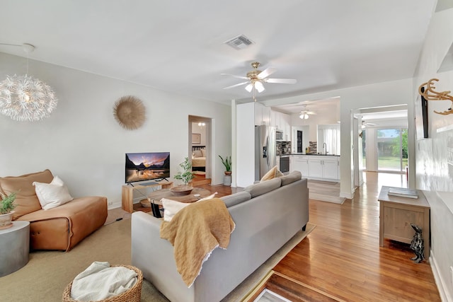 living area with an inviting chandelier, light wood-style flooring, visible vents, and baseboards