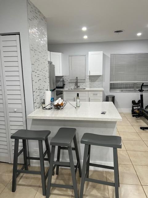 kitchen featuring a kitchen breakfast bar, light tile patterned floors, decorative backsplash, and white cabinets