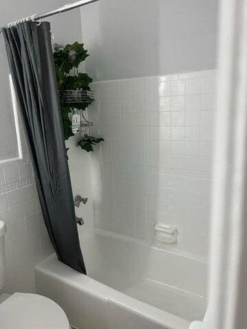 bathroom with toilet and shower / bathtub combination with curtain