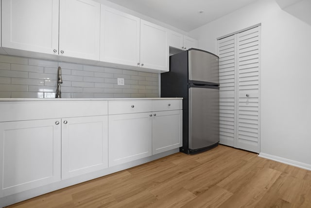 kitchen featuring white cabinets, light hardwood / wood-style floors, stainless steel refrigerator, sink, and decorative backsplash