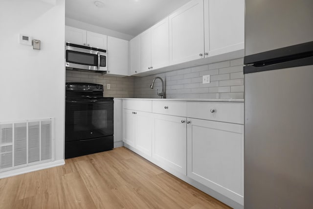 kitchen with tasteful backsplash, stainless steel appliances, sink, white cabinetry, and light wood-type flooring